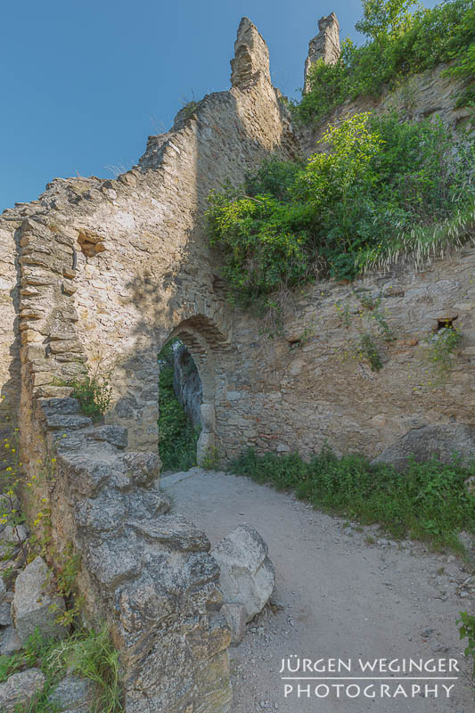 Pfad durch eine Burgruine mit verfallender Steinmauer und einem Torbogen. Burgruine Dürnstein ,Wachau, Niederösterreich.