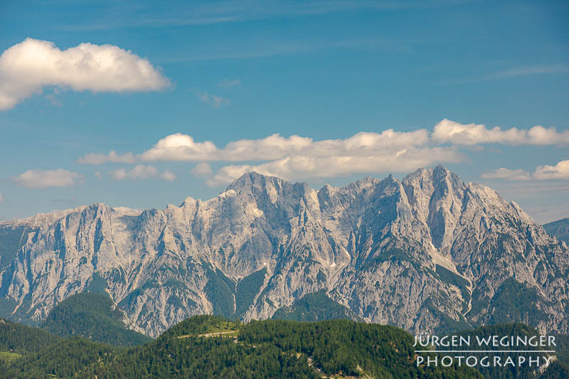 Berg mit blauem Himmel und weissen Wolken mit Wald im Vordergrund. Nationalpark Gesäuse