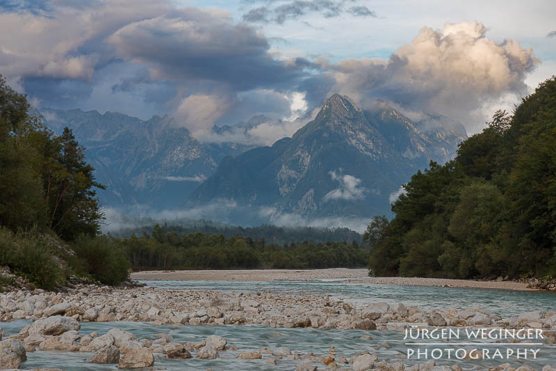 Gebirge mit Wolken mit Fluss im Vordergrund im Abendlicht. Julische Alpen, Rombon Kanin Gruppe, Triglav Nationalpark, Slowenien