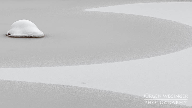 Zugefrorener See mit einem Schneebedeckten Stein und einem durch Schnee erzeugten Muster. Leopoldsteinersee, Steiermark